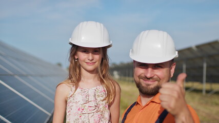 Wall Mural - Father with little girl at solar power plant. The father talks about solar energy. The concept of green energy will save the planet for children. The father puts a protective helmet on the girl's head