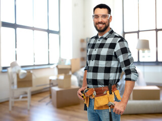 Wall Mural - repair, construction and building concept - happy smiling male worker or builder in goggles with tool belt over home room background