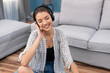 © ABCreative - An attractive brunette sits on the living room floor with wireless headphones on ears with hands on them. The teenager is listening to her favorite artist, a new album, relaxing with closed eyes
