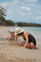 Wall Mural - Girl with her big sister building sand castle on the beach