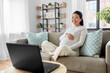 © Syda Productions - pregnancy, rest, people and expectation concept - happy smiling pregnant asian woman with laptop computer sitting on sofa at home