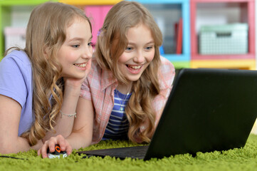 Two pretty little girls lying on floor and using laptop