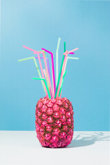 Wall Mural - Pink pineapple with colorful cocktail straws on sky blue background. Creative food composition. Party minimal concept.
