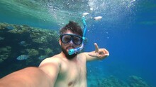 A Bearded Man Engaged In Scuba Diving Floats To The Surface Of The Sea Blowing Air Out Of A Breathing Tube And Shows A Victory Sign