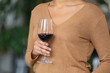 Portrait of unrecognizable woman with a glass of red wine in her hand. Mixed race female posing against blurred background of light room with green plants. Close up.