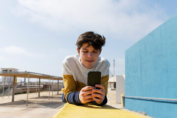 Young man using a smart phone texting messages , leaning on wall