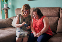 Adult Woman And Her Sister With Down Syndrome Look At A Phone At Home