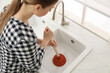 Young woman using plunger to unclog sink drain in kitchen, above view