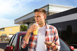 © New Africa - Young man with doughnut drinking juice near car at gas station