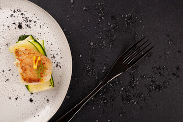 Wall Mural - Grilled fish fillet served with zucchini on white plate over black background.