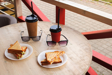 Two sandwiches, cup of coffee and sunglasses on table on terrace