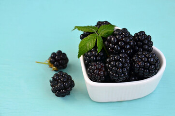 Wall Mural - Freshly picked organic blackberries in a white heart shaped bowl on a light blue background.Healthy eating,vegan food or diet concept.