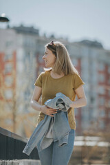 Sticker - Vertical shot of a young European lady smiling looking aside outdoors holding her jacket