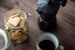 bote con galletas con forma de corazón, taza de café y cafetera sobre fondo de madera