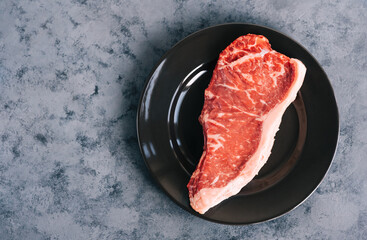 Wall Mural - Raw New York striploin beef steak in black plate on blue background with copy space.