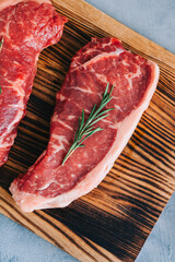 Raw New York striploin beef steak isolated on wooden board with rosemary.