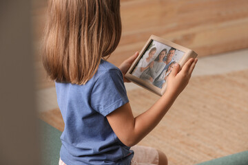 Poster - Little girl holding framed family photo indoors, closeup