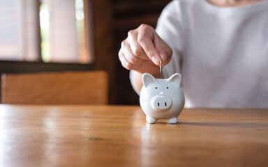 Wall Mural - Closeup image of a woman putting coins into piggy bank for saving money concept