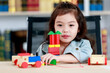 © Bangkok Click Studio - Lovely Asian girl enjoy playing toy and colorful wooden block and concentrate to stack each layer high as education of structure and balance skill while sitting on learning desk in home library