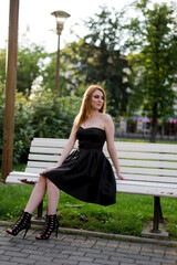 Sticker - Vertical grayscale shot of a young Caucasian lady in an elegant dress and look sitting on a bench