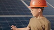 © GRAFStock - Little boy in a protective helmet at a solar power plant. The concept of children and green energetics. Children for clean energy. Shooting at a solar power plant. Ecological farm. Solar power station