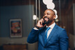 Portrait smiling african american businessman in blue suit in office with mobile phone speaking talking smiling indoor