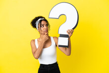 Young African American Woman Isolated On Yellow Background Holding A Question Mark Icon And Having Doubts