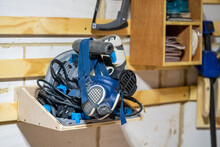  selected focus close up of a blue respirator hanging off an electric power tool plunge saw sitting on a shelf mounted to a french cleat system