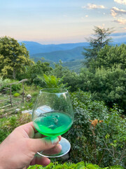 Canvas Print - Verre d'apéritif tenu en main devant un paysage de montagne, Cévennes