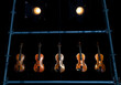 Five violins or violas hanging within a steal bar frame with two stage lights creating some ambient mood