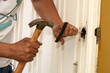 man installing a lock with a screwdriver and hammer