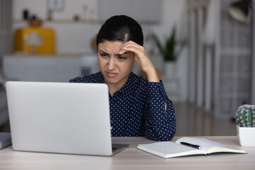 Wall Mural - Unhappy millennial Indian woman sit at table at home office feel bored unmotivated working online on laptop. Upset young biracial female study distant on computer, lack motivation at workplace.