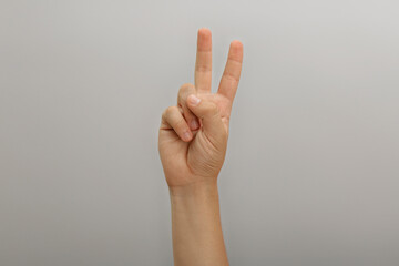 Teenage boy showing two fingers on light background, closeup