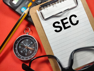 Text SEC (Securities Exchance Comission) writing on clip board with compass,pencil,calculator and glasses on red background.