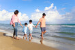 © Stella - Happy family of four spend time together on summer holiday vacation, parents and children holding hand and walking along tropical sea beach, mother father and kids resting and relaxing on weekend