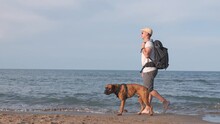 Traveling Man With His Boxer Dog Walking On The Beach