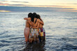 three young latin women hug each other in the water at sunset, showing friendship or sisterhood