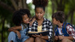© SHUTTER DIN - Sister black skin African American ethnicity sitting at on tree base nature reading to her younger siblings a book about adventure stories