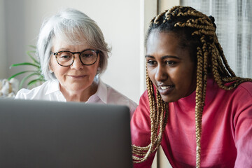 Diverse senior and young woman having video call on laptop computer at home office - Focus on african girl