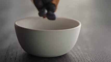 Wall Mural - Slow motion ripe blueberries fall in white bowl on oak table