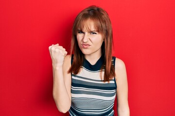 Wall Mural - Redhead young woman wearing casual t shirt angry and mad raising fist frustrated and furious while shouting with anger. rage and aggressive concept.