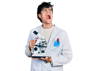 Sticker - Handsome hipster young man wearing lab coat holding microscope angry and mad screaming frustrated and furious, shouting with anger looking up.