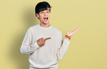 Handsome hipster young man wearing casual winter sweater amazed and smiling to the camera while presenting with hand and pointing with finger.