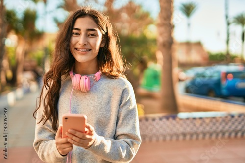 Young middle east girl smiling happy using smartphone and headphones at the city.