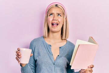 Sticker - Beautiful blonde woman reading a book and drinking a cup of coffee angry and mad screaming frustrated and furious, shouting with anger looking up.