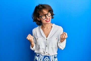 Sticker - Young brunette woman wearing casual clothes and glasses very happy and excited doing winner gesture with arms raised, smiling and screaming for success. celebration concept.