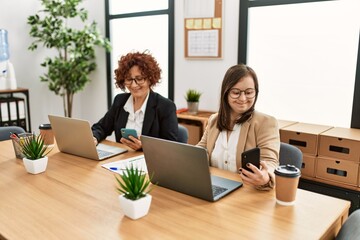 Group of two women working at the office. Mature woman and down syndrome girl working at inclusive teamwork.