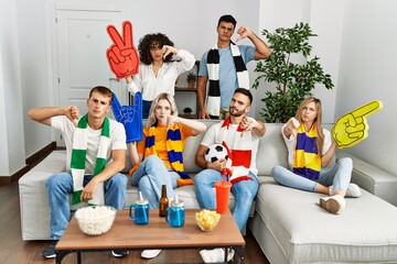 Sticker - Group of friends supporting football team watching tv al home sitting on the sofa with angry face, negative sign showing dislike with thumbs down, rejection concept