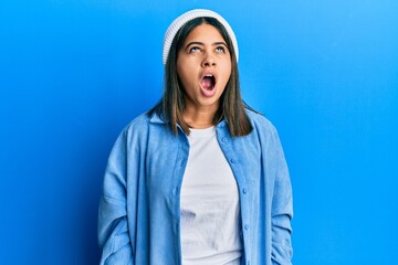 Poster - Young latin woman wearing cute wool cap angry and mad screaming frustrated and furious, shouting with anger. rage and aggressive concept.