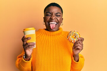 Sticker - Young african american woman eating doughnut and drinking take away coffee sticking tongue out happy with funny expression.